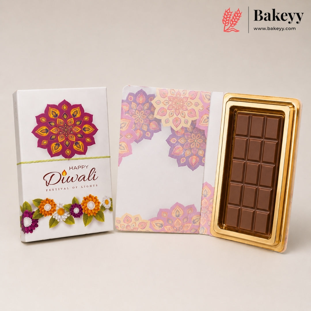 A boxed Diwali chocolate gift set on a light beige background. The set includes a white box with a colorful mandala design and 'Happy Diwali' text, a matching patterned envelope, and a gold-trimmed chocolate bar in a gold tray.