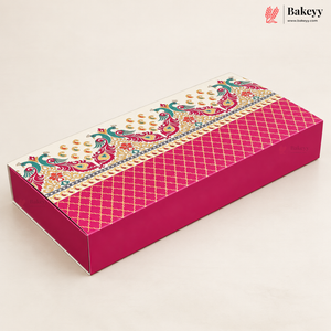 A rectangular pink bakery box with a decorative patterned lid, photographed on a clean off-white background. The box features a bright pink body with a gold lattice pattern and a white patterned top band with teal and gold motifs.