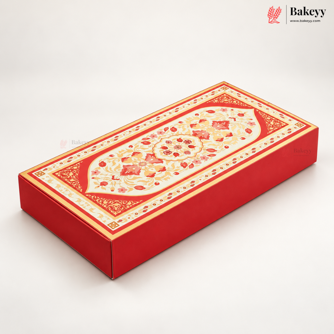 A rectangular red bakery gift box with ornate gold and cream floral patterns on the lid, photographed on a clean white background. A Bakeyy logo watermark is visible in the top right corner.