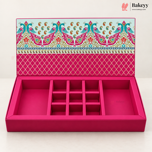 An open pink jewelry box with multiple compartments and a decorative patterned lid, photographed on a clean white background. The Bakeyy logo appears in the top right corner.