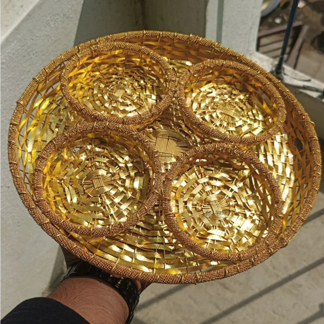 Hand holding a round golden dry fruits tray with five woven compartments, ideal for gift hampers