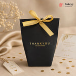 Black gift bag with yellow ribbon and 'THANK YOU' text on a beige background with decorative elements.