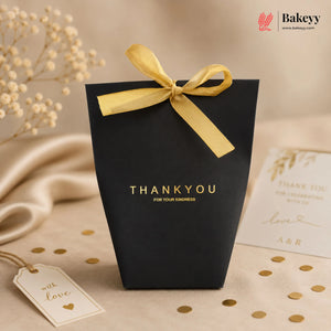 Black gift bag with yellow ribbon and 'THANK YOU' text on a beige background with decorative elements.