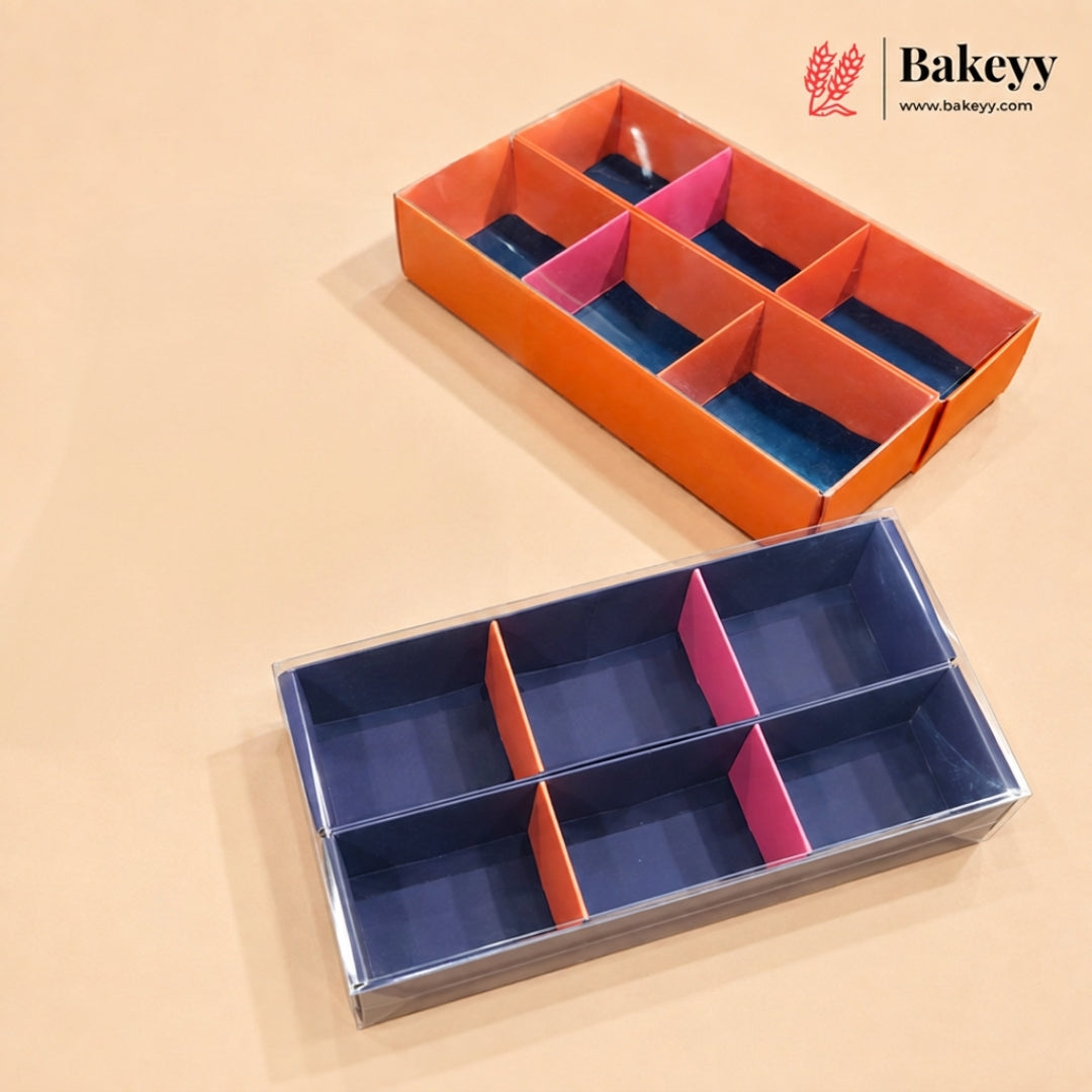 A six-compartment bakery box shown in two color configurations: one with an orange exterior and pink and blue interior dividers, and another with a navy blue exterior and pink and orange interior dividers, displayed on a beige background with the Bakeyy logo in the top right corner.