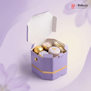 Hexagonal purple gift box with gold accents containing pastries on a light purple background, featuring the Bakeyy brand.