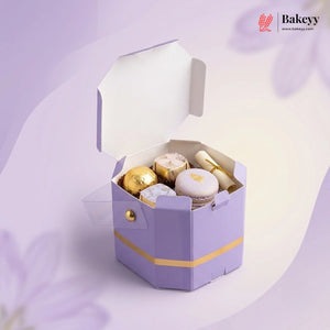 Hexagonal purple gift box with gold accents containing pastries on a light purple background, featuring the Bakeyy brand.