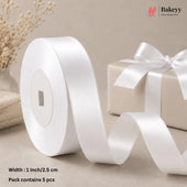 A roll of white satin ribbon with a matching ribbon on a gift box, styled on a beige surface with dried flowers and a gift box in the background. Text at the bottom left reads 'Width : 1 Inch/2.
