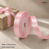 A roll of light pink satin ribbon with a matching bow on a brown kraft paper gift box, set against a neutral beige background. Text at the bottom left specifies the width as 1/2 inch (1.