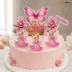 A pink fairy-themed birthday cake decorated with a large pink butterfly topper, a gold crown, three pink fairy cutouts, mushroom toppers, and a small 'Happy Birthday' sign on a white plate.