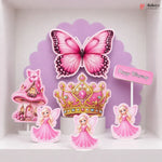A set of pink fairy-themed birthday cake toppers displayed on a white shelf against a purple scalloped backdrop. The set includes a large pink butterfly, a pink and gold tiara, three fairy figures in pink dresses, a pink castle, and a small 'Happy Birthday' sign.