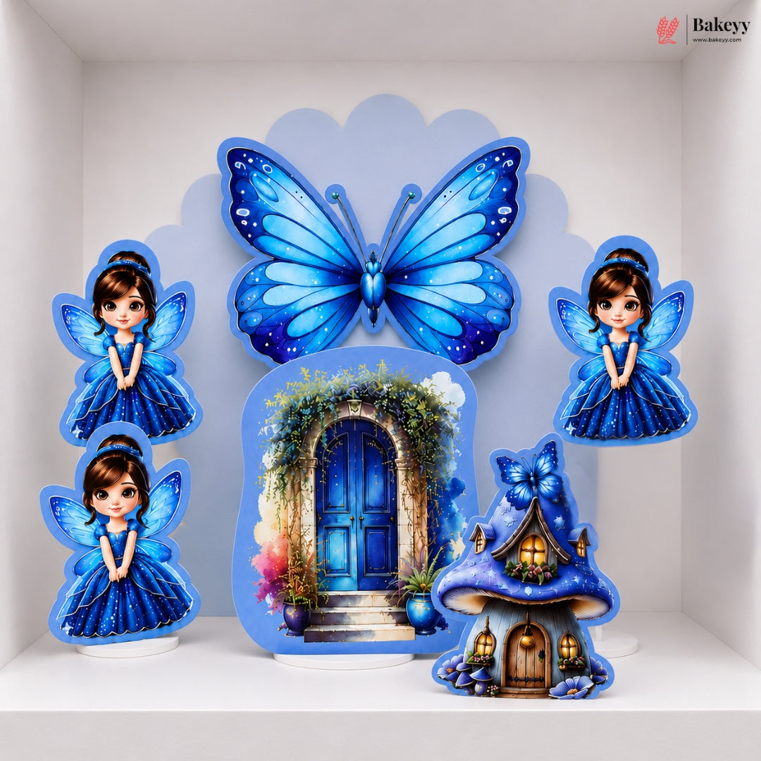 A set of blue fairy-themed decorative wall cutouts and a small fairy house, displayed on a white shelf against a white wall. The set includes a large butterfly, two fairy figures, a blue door arch print, and a glowing fairy house with a blue bow.
