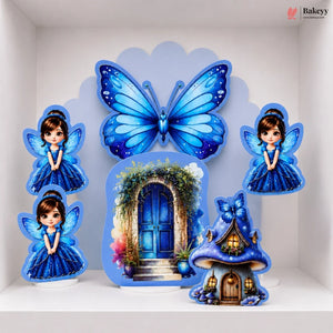 A set of blue fairy-themed decorative wall cutouts and a small fairy house, displayed on a white shelf against a white wall. The set includes a large butterfly, two fairy figures, a blue door arch print, and a glowing fairy house with a blue bow.