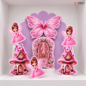 A set of pink fairy-themed party decorations displayed on a white shelf, including a large butterfly, a floral fairy door, two mushroom houses, and two fairy cutouts.