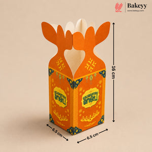 An orange cardboard gift box with a festive Golu design, featuring antler-like tabs at the top, decorated with yellow and blue patterns. The image includes dimension markings showing 16 cm height and 6.