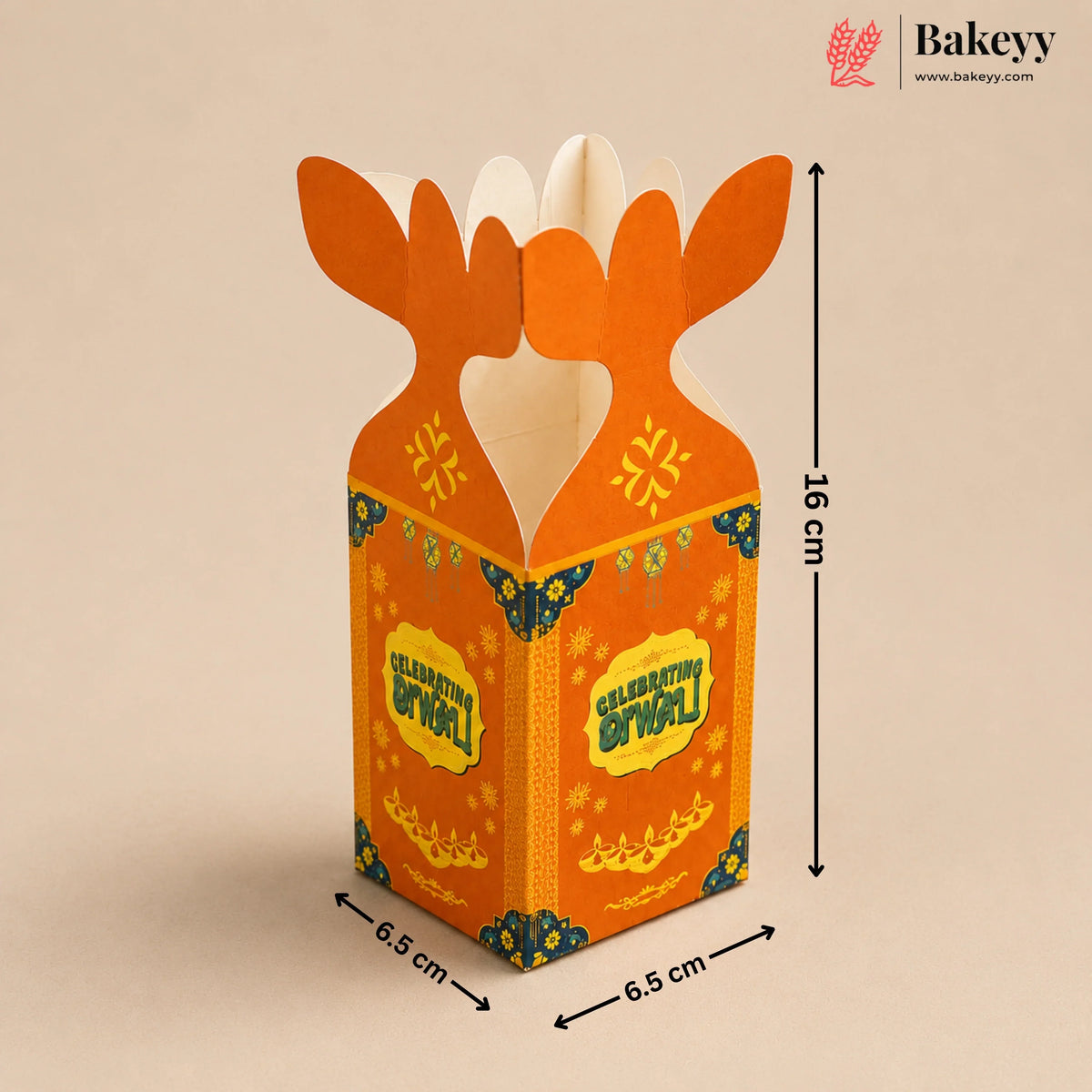 An orange cardboard gift box with a festive Golu design, featuring antler-like tabs at the top, decorated with yellow and blue patterns. The image includes dimension markings showing 16 cm height and 6.