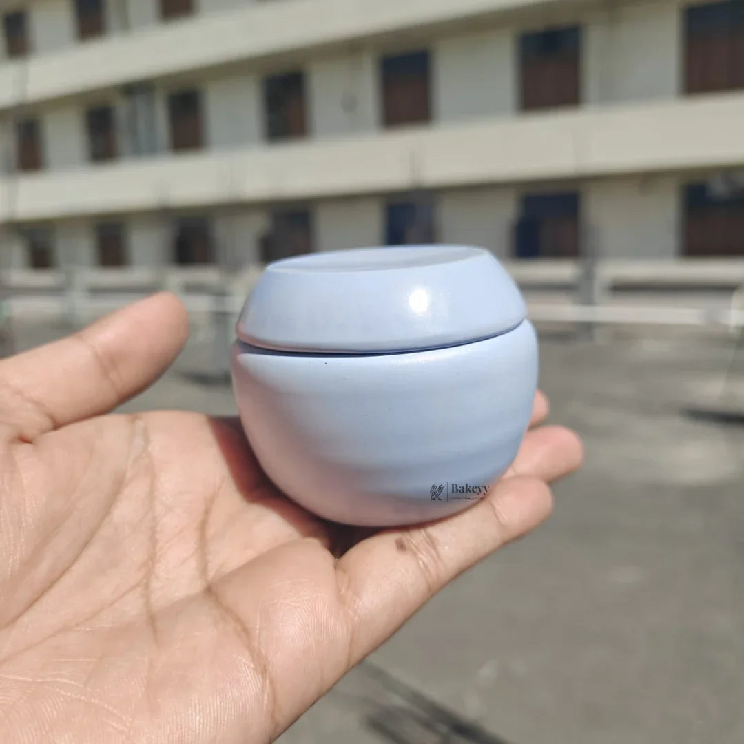 Light blue round tin box with flat top held in hand, Bakeyy gift packaging container