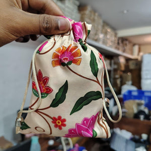 Hand holding a drawstring bag with floral embroidery in a blurred indoor setting
