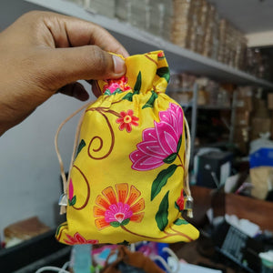 Hand holding a yellow fabric pouch with floral patterns in a blurred indoor setting