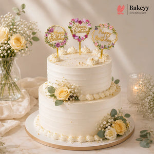 White birthday cake with floral decorations and 'Happy Birthday' toppers on a light background.