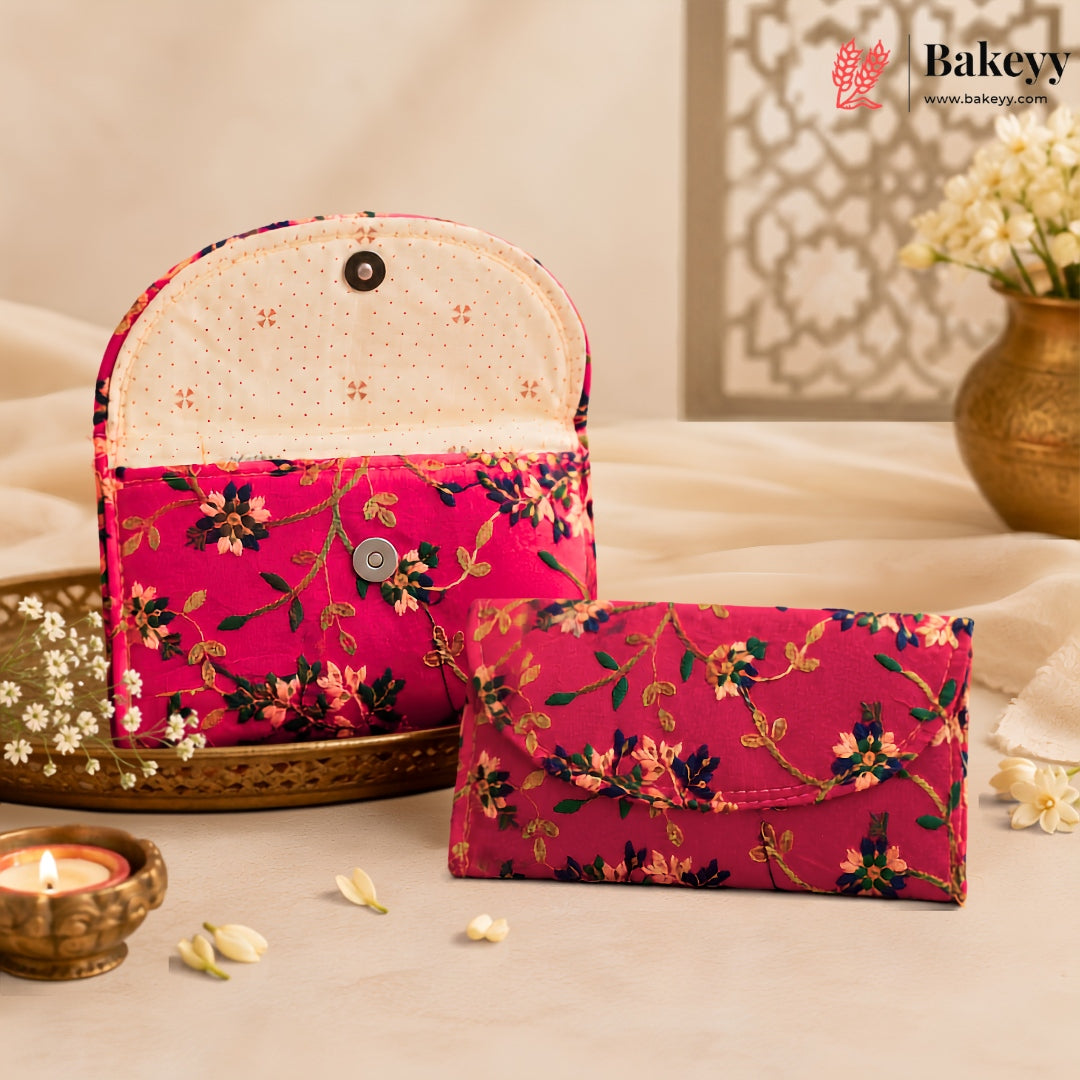 A pink floral fabric clutch wallet and matching envelope-style card holder displayed on a beige surface with decorative props including a candle, tray, flowers, and a vase. The Bakeyy brand logo appears in the top right corner.