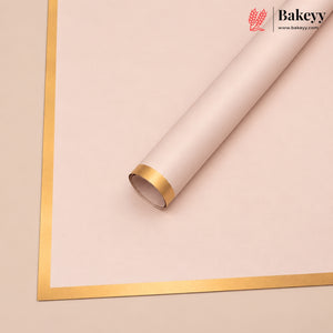 A roll of pale blush pink bakery wrapping paper or backdrop sheet with a metallic gold border, shown on a matching light beige background. The Bakey brand logo is visible in the top right corner.