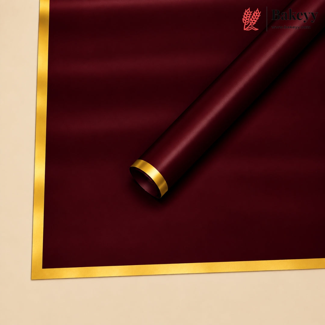 A roll of deep burgundy wrapping paper with a metallic gold border, shown partially unrolled on a light beige background. The Bakeyy logo is visible in the top right corner.