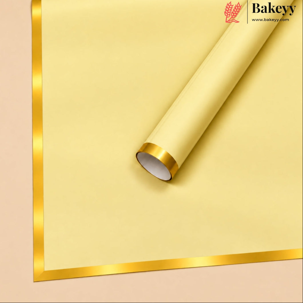 A roll of pale yellow bakery paper or wrapping paper with a shiny gold metallic border, shown partially unrolled on a light beige background. The Bakeyy brand logo is visible in the top right corner.