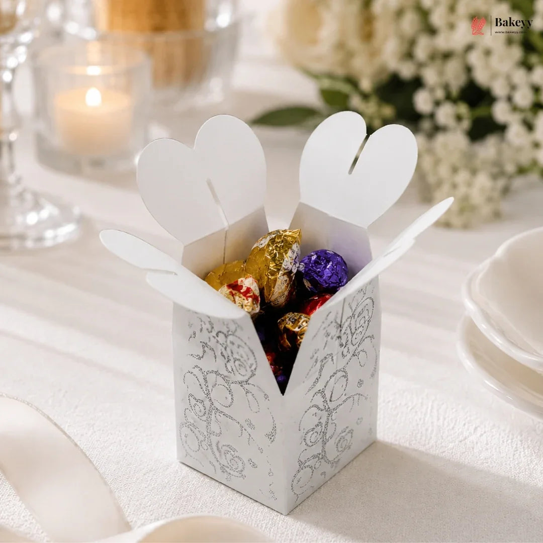 White decorative box with heart-shaped flaps containing colorful candies on a white surface.