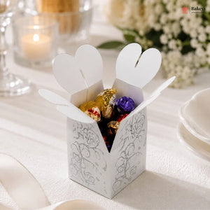 White decorative box with heart-shaped flaps containing colorful candies on a white surface.