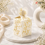 Decorative white box with gold patterns on a marble surface with flowers.