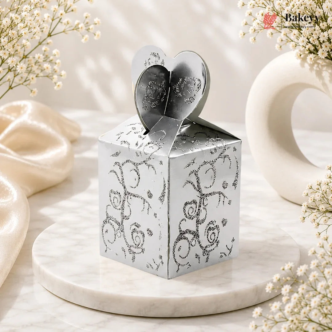 Silver decorative box with heart-shaped lid on a marble surface with flowers.