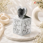 Silver decorative box with heart-shaped lid on a marble surface with flowers.