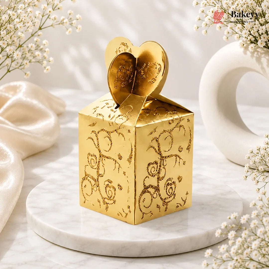Gold decorative box with heart design on top, placed on a marble surface with white flowers.