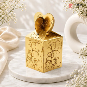 Gold decorative box with heart design on top, placed on a marble surface with white flowers.
