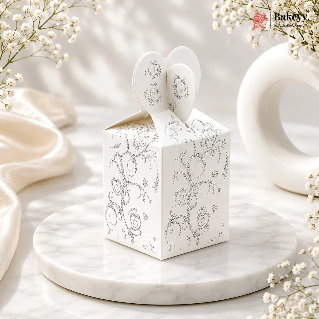 White decorative box with heart design on top, placed on a marble surface with floral elements.