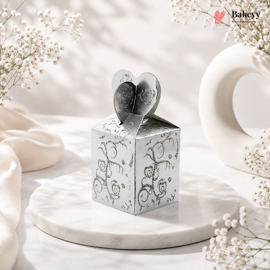 Silver decorative box with heart-shaped lid on a marble surface with white flowers.