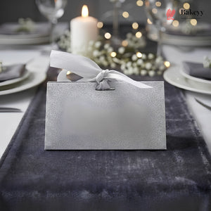 Silver tissue box with a bow on a table setting with candles and lights in the background