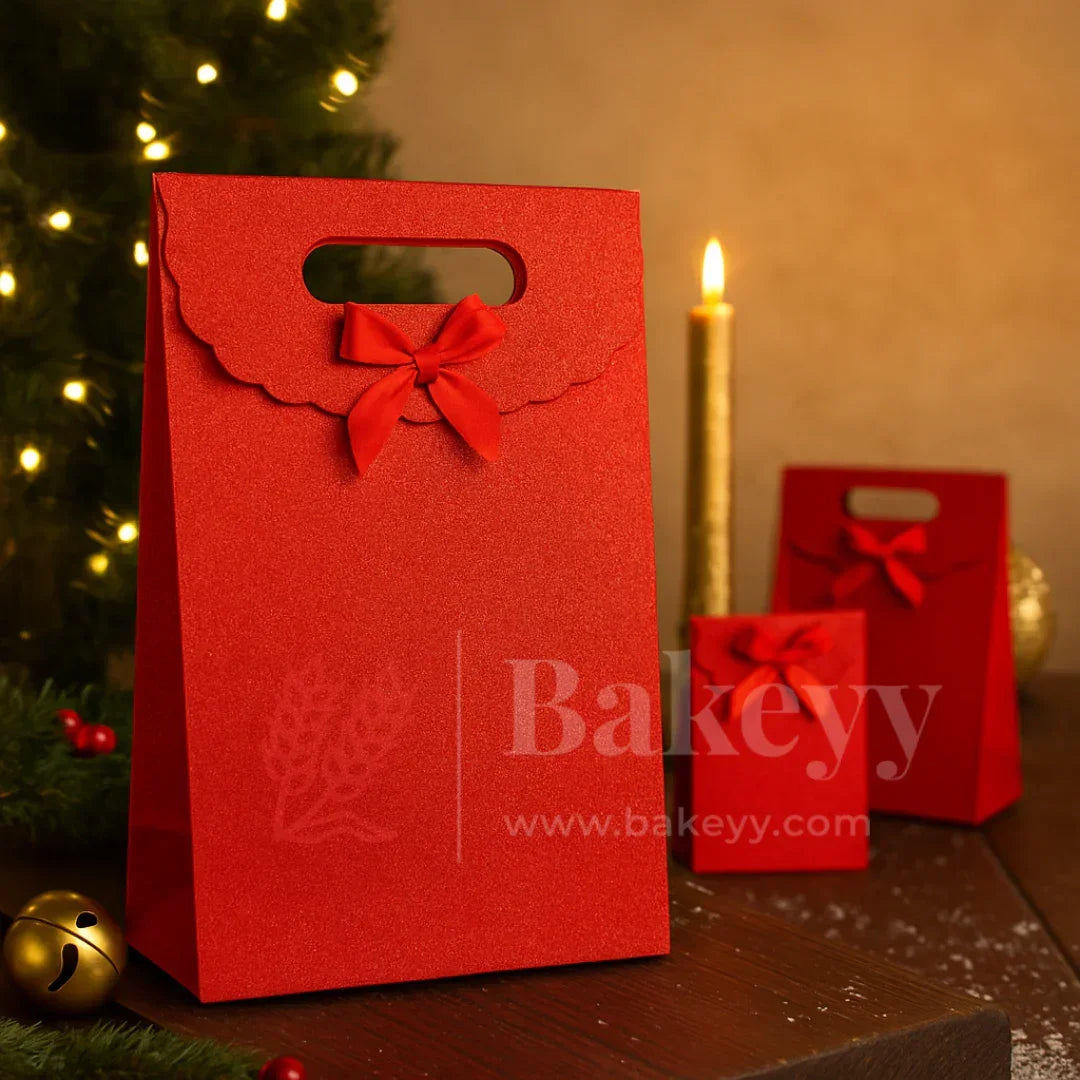 Red gift bag with a bow on a wooden surface with a Christmas tree and candle in the background, featuring the brand 'Bakeyy'.