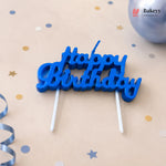 Blue 'Happy Birthday' cake topper on a beige background with confetti and ribbons.