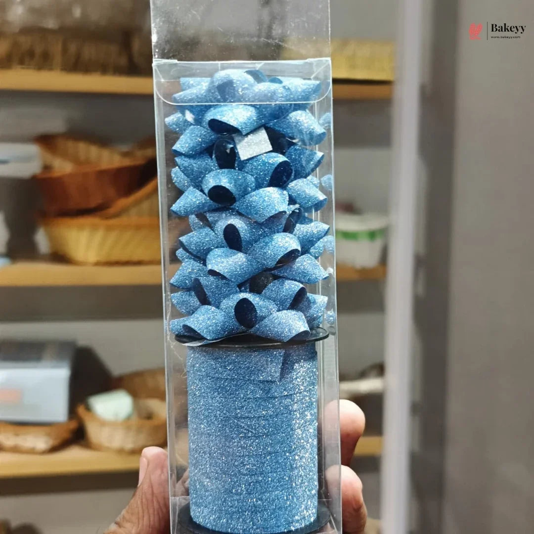 Blue glittery cake topper in a clear packaging tube held by a person.