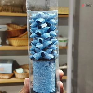 Blue glittery cake topper in a clear packaging tube held by a person.