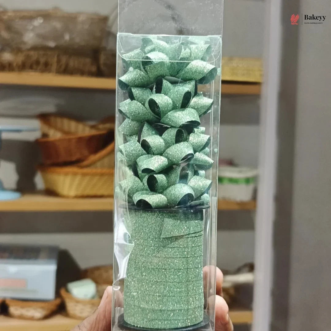 Green glittery ribbon roll in a clear packaging held by a hand with a blurred background.