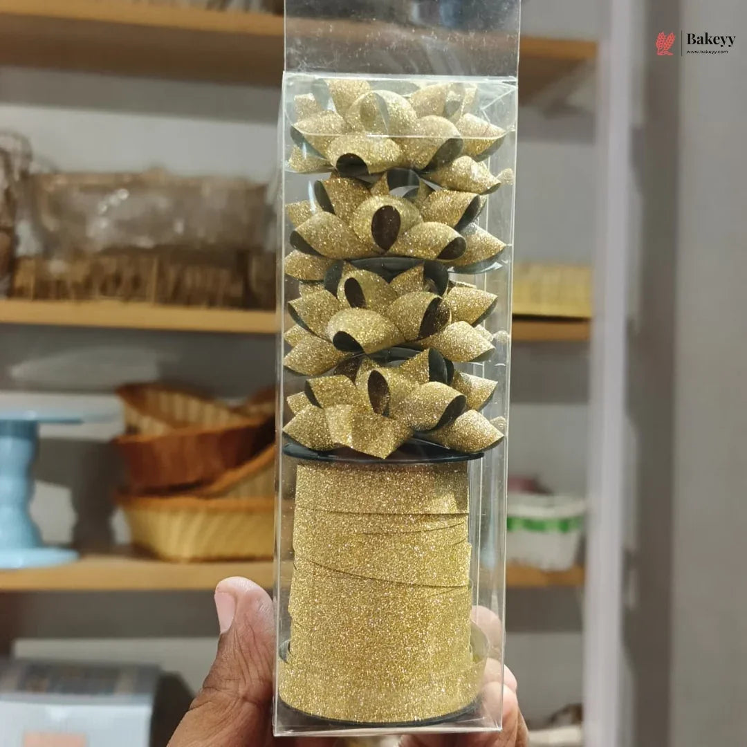 Gold glittery cake decorations in a clear packaging tube held by a hand with a blurred background.