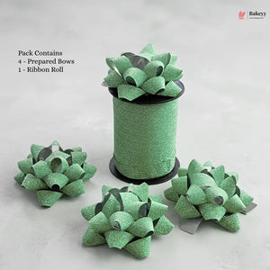 Green glittery bows and a roll of ribbon on a light gray background with 'Bakeyy' branding.