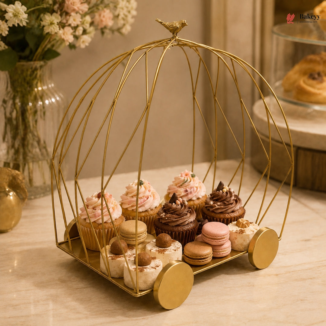 Decorative gold birdcage with cupcakes and macarons on a table.