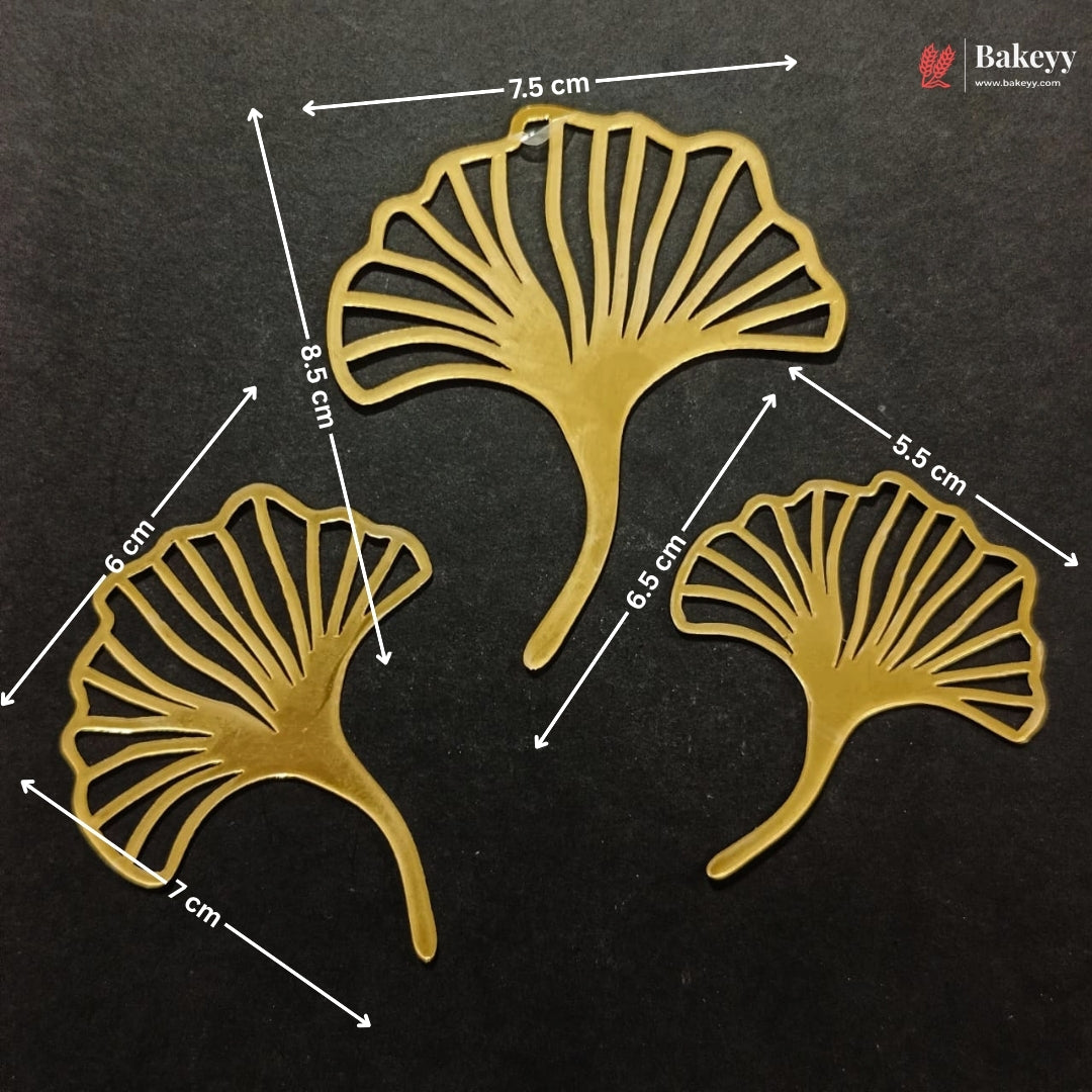 Three gold-colored metal ginkgo leaf cutouts displayed on a black background with white dimension arrows and labels indicating measurements in centimeters. A Bakeey logo is visible in the top right corner.