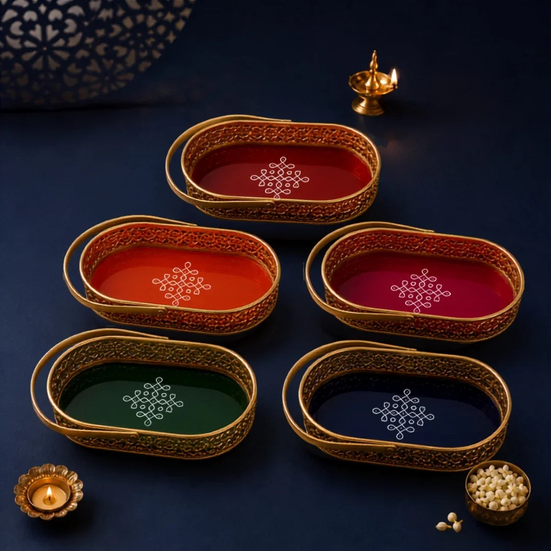 Six oval decorative trays with gold-toned filigree borders and colorful interiors are arranged on a dark navy surface. The trays are in red, orange, magenta, green, and navy blue, each with a white geometric motif in the center.