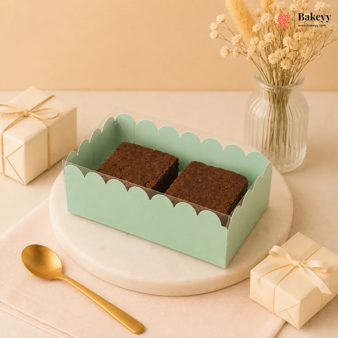 Two brownies in a green box on a decorative table with a spoon and small gift boxes.