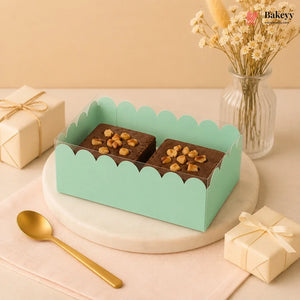 Two chocolate desserts with nuts in a green box on a decorative table with a gift and vase.