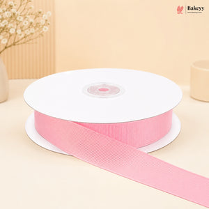 A spool of light pink grosgrain ribbon with a length draped out in front, set against a warm beige background with soft decorative props.